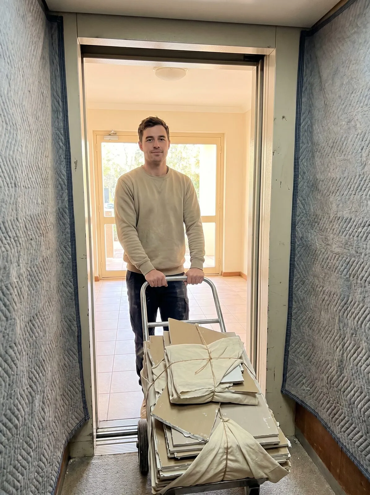 A crew member steadying a trolley of wrapped plasterboard inside a lift lined with protective blankets