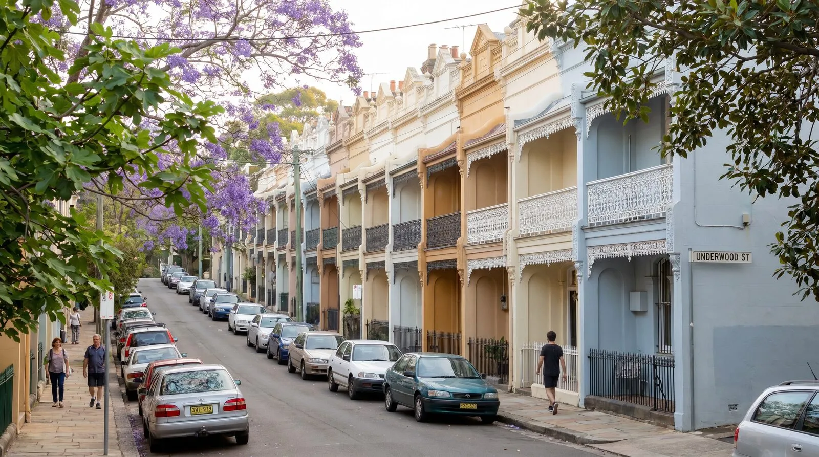 A steep Paddington street of painted terrace houses with iron lace balconies, cars parked along both kerbs